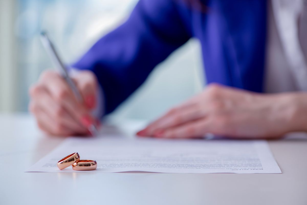 The Benefits of a Prenuptial Agreement - Image of a woman signing paperwork and wedding bands are in the foreground