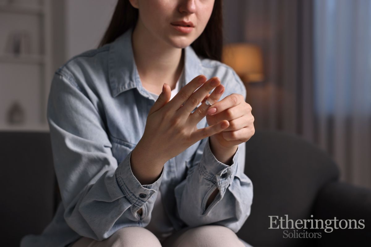 Woman taking off her engagement ring, looking sad.