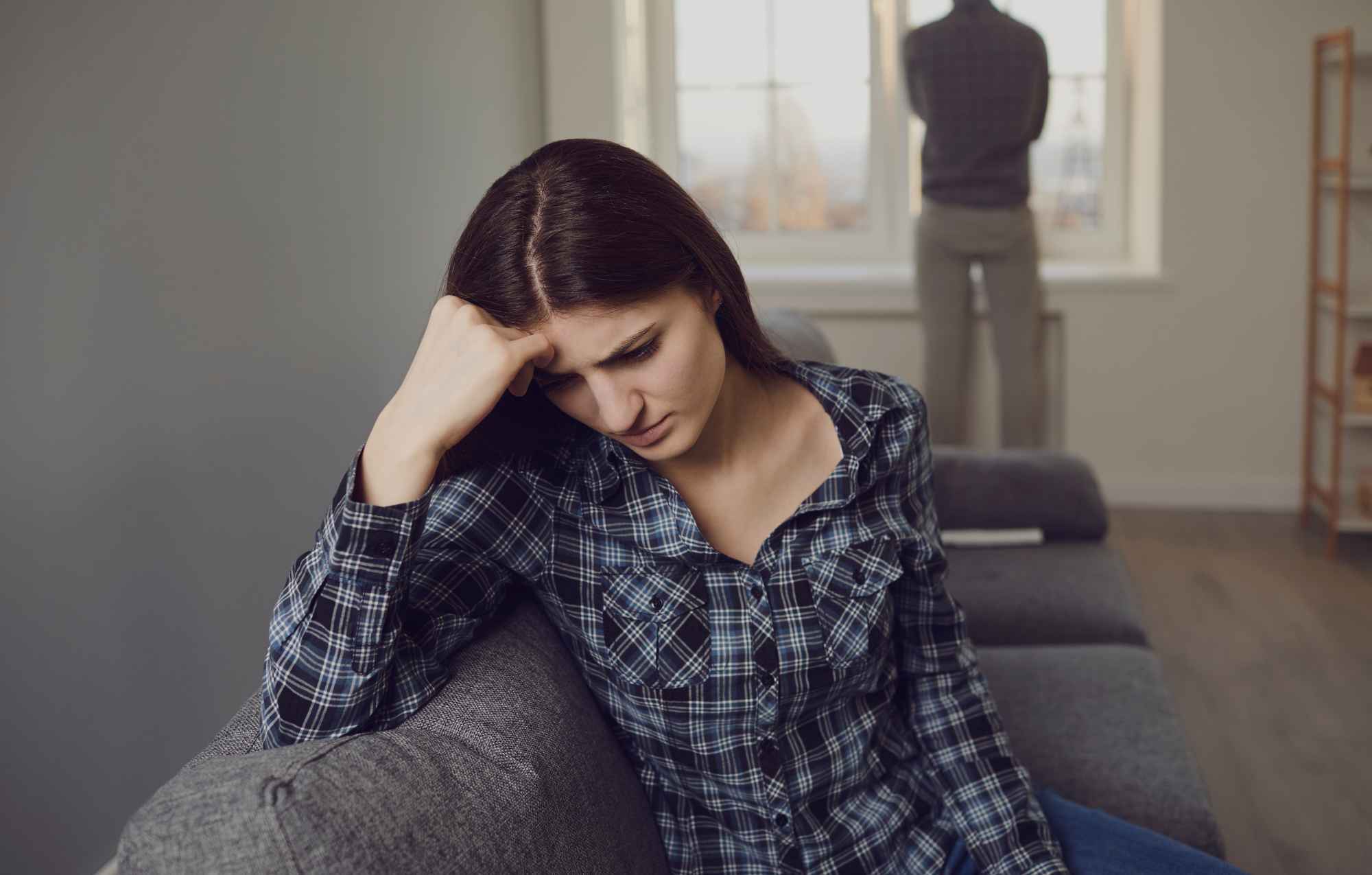 Woman looking distressed while an angry man stands blurred in the background